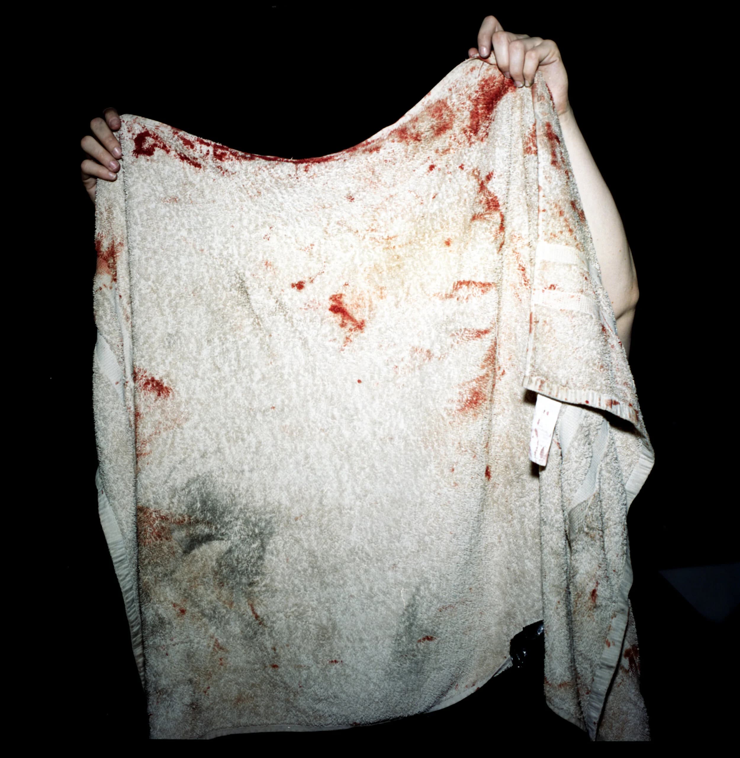 A pair of hands holding up a bloodstained white towel against a black background