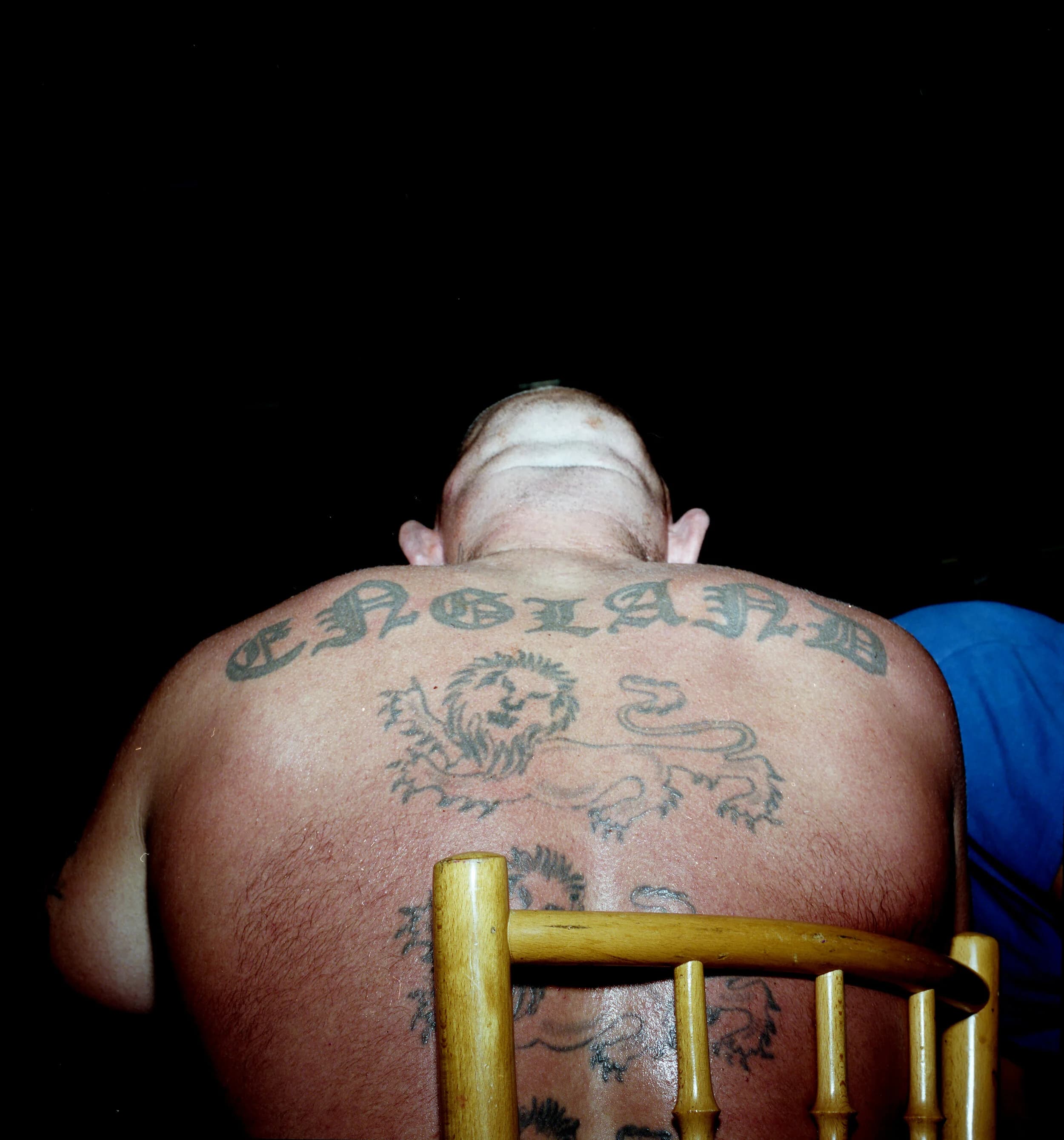 Man seated with his back to the camera, ENGLAND in old English lettering and heraldic lions tattooed across his back
