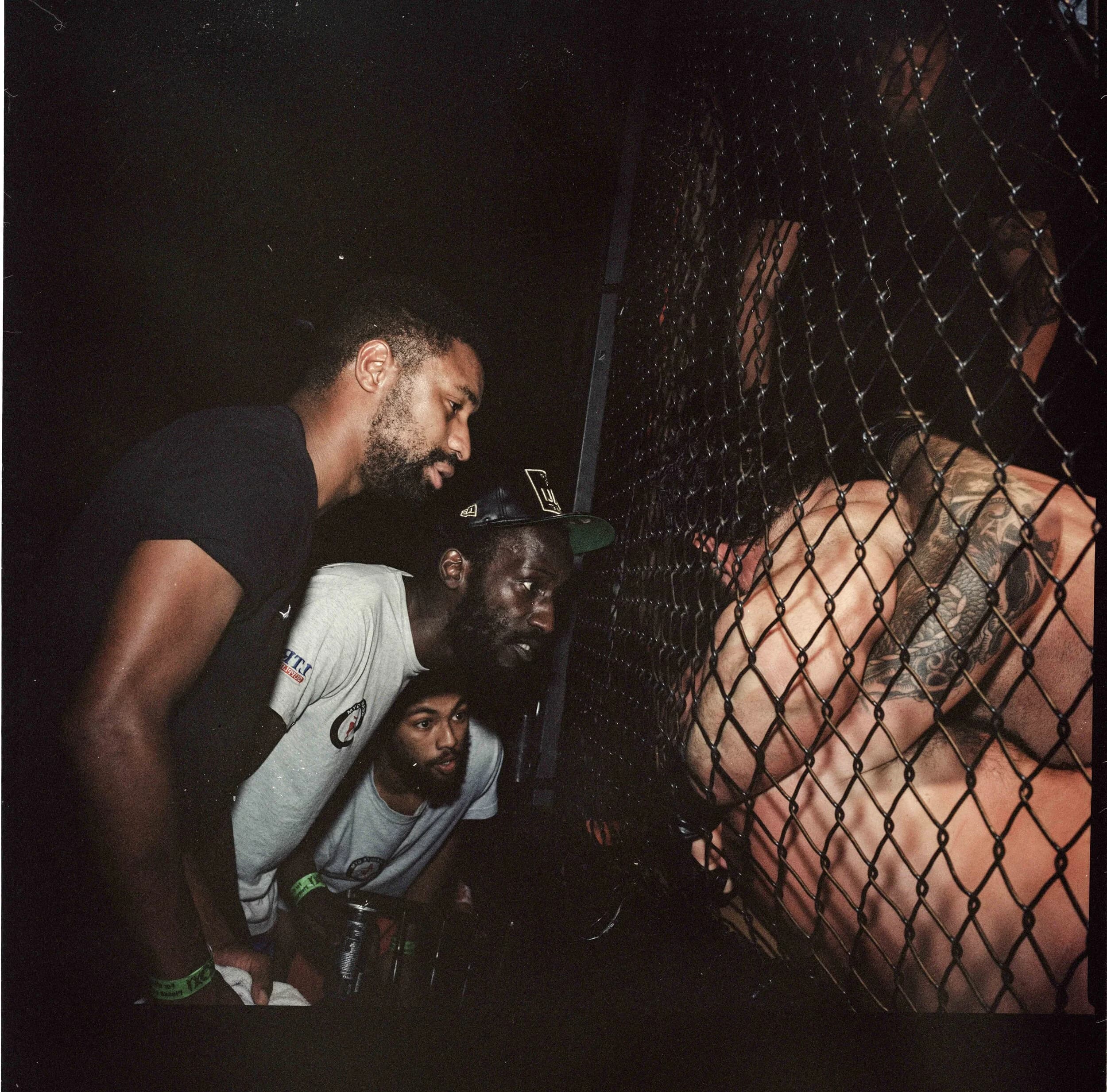 Post-fight portrait of a wide-eyed fighter with a bright red mouthguard between his lips and a Celtic cross tattooed on his chest